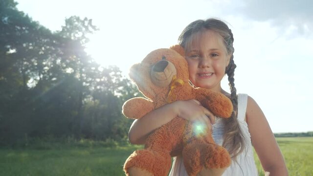 little kid girl hugging a teddy bear toy portrait in the park in nature. childhood dream concept. smiling kid child with favorite toy teddy bear dream of happiness in a green park lifestyle outdoor