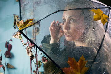 sad woman wipes tears under a transparent umbrella with raindrops with autumn leaves. Soft focus