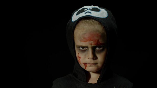 Halloween, angry girl with blood makeup on face. Kid dressed as scary skeleton, posing, making faces