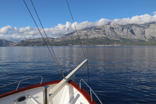 Seascape view of high mountains covered with white clouds, sea coast, blue sea and clear sky from the board of a pleasure yacht ship on a sunny summer day, Croatia