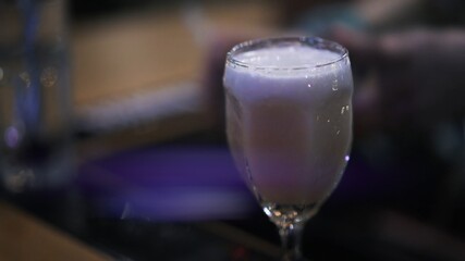 Cocktail in glass on blurry background in the bar, lens flare. Close up of a cocktail made in bar, on background of violet night light inside