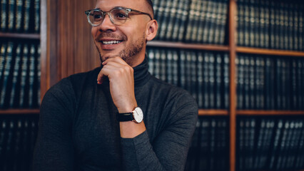 Cheerful male lecturer in optical eyeglasses for vision protection standing in archive space and...
