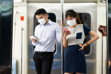 Asian young woman use smart phone on Public Transport. Crowd of passengers on Urban Public Transport Metro. Face Mask protection against virus. Covid-19, coronavirus pandemic