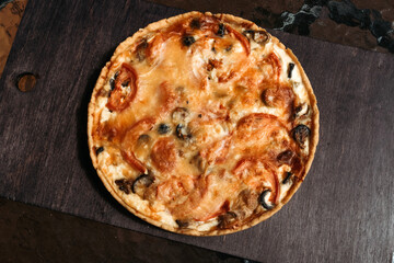 Large pie with cheese and vegetables for whole family. Cakes from cafe. Homemade pie on black background. Pie and pepper shaker with cutlery on table in cafe. Early morning, holiday with cake in cafe.