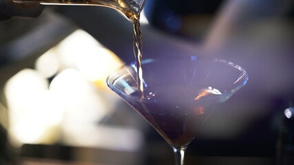 Bartender pouring whiskey into cocktail glass, close up shot in a bar. Pouring cocktail into small glass, cocktail preparation concept, blurry background