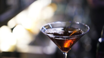 Whiskey in a cocktail glass, close up shot in a bar, bokeh lights. Cocktail into small glass, cocktail preparation concept, blurry background
