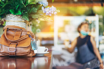 Mini alcohol gel bottle to kill Corona Virus(Covid-19) hang on a brown leather shoulder bag with hot coffee on table in cafe.New normal lifestyle.Health care concept.Selective focus on alcohol gel