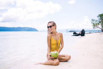 Young smiling blonde sitting on beach with pina colada in coconut