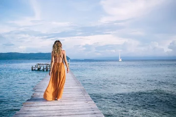 Crédence de cuisine en verre imprimé Zanzibar Vue arrière d& 39 une touriste profitant de vacances dans un lieu de villégiature dans un environnement naturel paradisiaque, femme en robe d& 39 été élégante marchant sur la jetée se recréant pendant un voyage en solo pour visiter l& 39 île de Bora Bora