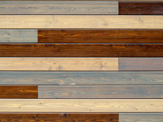 The wall is covered with long planks. The cladding boards are varnished and have different colors. The planks are arranged in neat rows. Background with wooden planks
