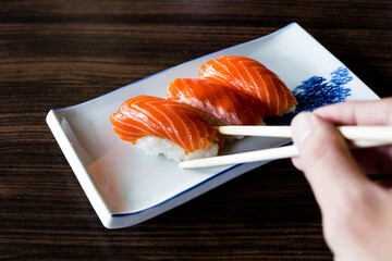 Hand holding Salmon sushi with chopsticks on  wooden table