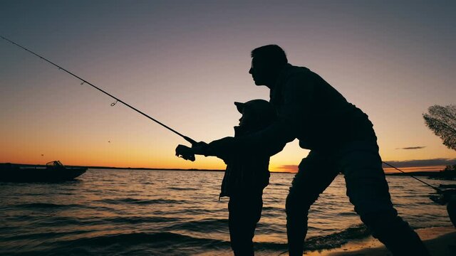 A man is helping his son with fishing at sunset