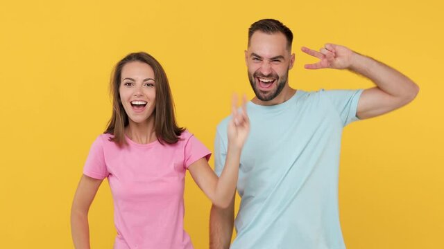 Young couple friends bearded man woman 20s in basic t-shirts posing isolated on yellow background studio. People lifestyle concept. Dancing fooling around having fun expressive gesticulating hands