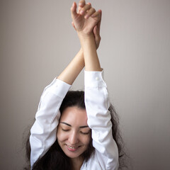 Portrait of young woman with brunette curly hair in a white shirt over simple background.