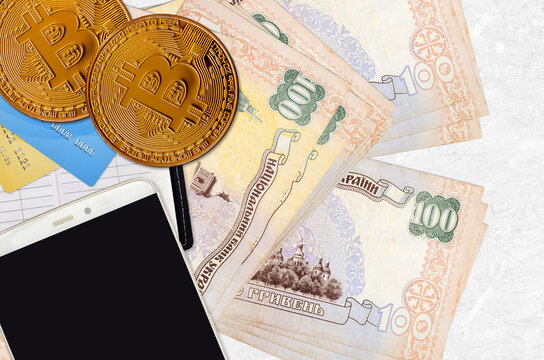 100 Ukrainian hryvnias bills and golden bitcoins with smartphone and credit cards. Cryptocurrency investment concept. Crypto mining or trading