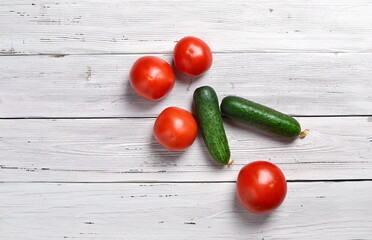 close up of red tomatoes and green cucumbers on an old wooden light rustic table