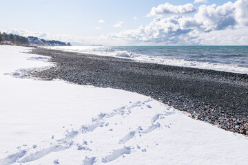 Steps on white snow leading to the rocky beach and sea in the background. Holidays in Batumi.  Global warming and mix of seasons.