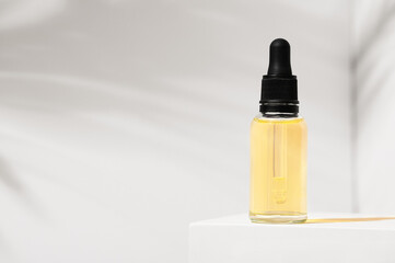 Serum bottle with dropper on white stand and background with palm shadow. Skincare beauty spa...