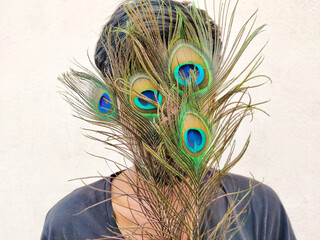 South Indian man covering his face with beautiful peacock feathers. Isolated on black background.