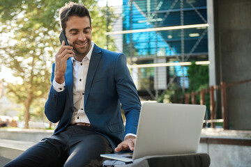 Businessman using a laptop outside and talking on his cellphone