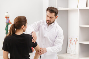 Fototapeta premium Male doctor examining female patient suffering from elbow pain. Medical exam. Chiropractic, osteopathy, post traumatic rehabilitation,sport physical therapy. Alternative medicine, pain relief concept.