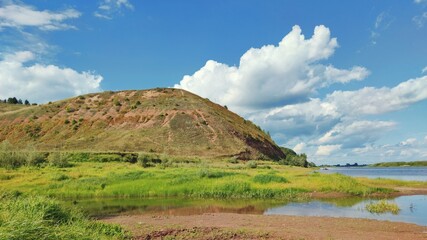 mountain near the river on a background of blue sky with clouds on a sunny day