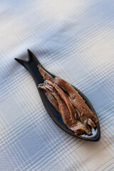 Vertical shot of anchovies caught in the Cantabrian Sea plated in a blue fish shaped plate served on a blue squared tablecloth. Anchovy is a typical high quality tapas dish from the northern Spain.