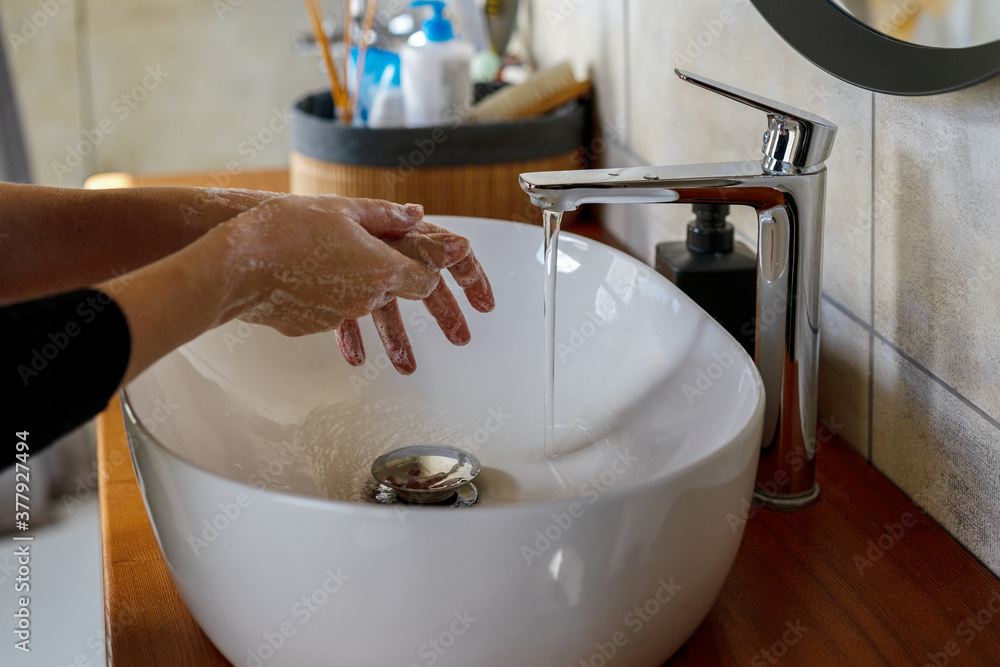 Wall mural woman washing hands with soap and running warm water over the sink. coronavirus prevention concept.