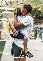 Sad young blond boy crying on fathers hands in nature park outdoor. Man holds son, hugs and...