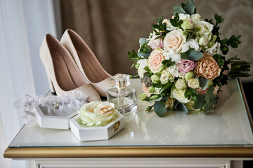 Obraz na płótnie Canvas bridal accessories such as shoes, bouquet , ring and parfume on a table