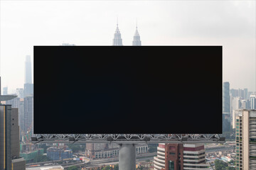 Naklejka premium Blank black road billboard with Kuala Lumpur cityscape background at day time. Street advertising poster, mock up, 3D rendering. Front view. Concept of marketing to promote or sell services or ideas.