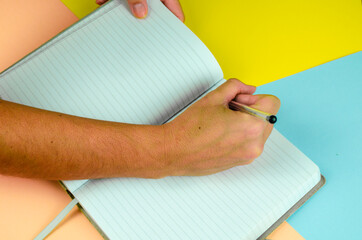 mano tomando notas en una libreta con fondo liso de colores