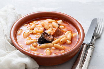 typical spanish dish fabada, beands with smoked sausages and meat on brown ceramic dish