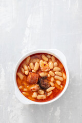 typical spanish dish fabada, beands with smoked sausages and meat on white dish