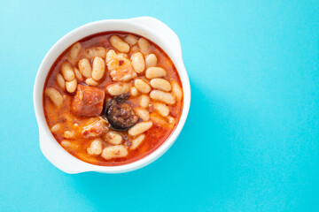 typical spanish dish fabada, beands with smoked sausages and meat on white bowl