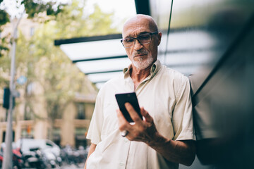 Serious bearded adult man using smartphone on street