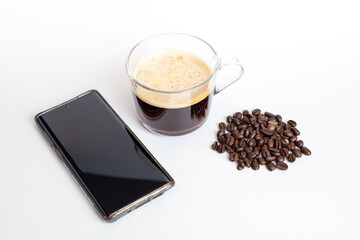 A glass of coffee grinder with coffee beans and black screen mobile phone on white background