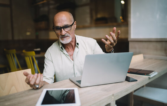 Bewildered Aged Businessman Working Remotely In Cafe