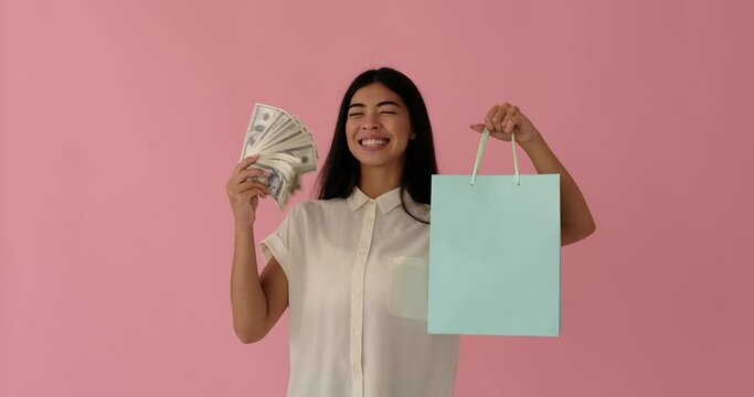Excited woman holding bundle of dollar banknotes and showing her shopping bags