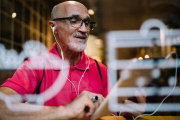 Smiling senior man surfing internet in earphones