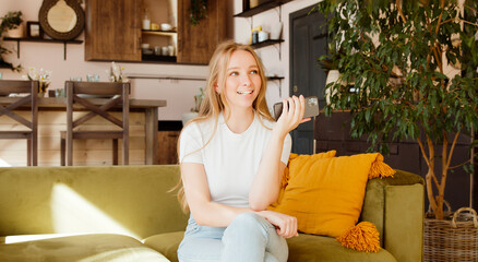 Smiling young woman recording voice message, dictates thoughts. Blonde lady record voice answer in...