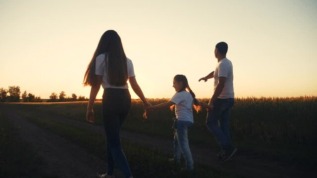 happy family fun walks at sunset in the field with wheat. mom dad and girl kid daughter walk outdoor in the park sunset silhouette. parents and child together are walking. people in the park lifestyle