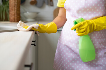 Cleaning service, house keeping. Hygiene and cleanliness in the kitchen. The girl in yellow rubber gloves and an apron removes. Hand wipes the table surface and holds the spray