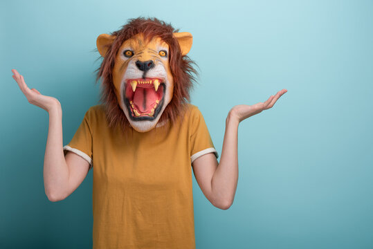 Confused young woman in lion mask standing and shrugging shoulders