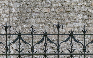 fragment of a stone wall of a very old building with an iron fence