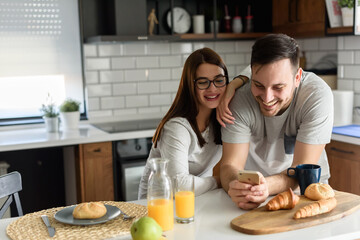 Smiling couple enjoying a beautiful morning at home kitchen, having breakfast, drinking coffee and...