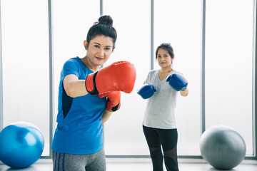 Pair of women in sportswear is exercising with boxing punches and jumping at the modern gym. She...