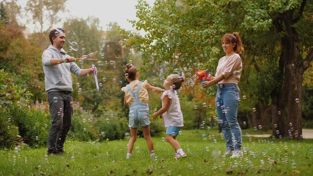 Parents and kids having fun together with soap bubbles in summer park