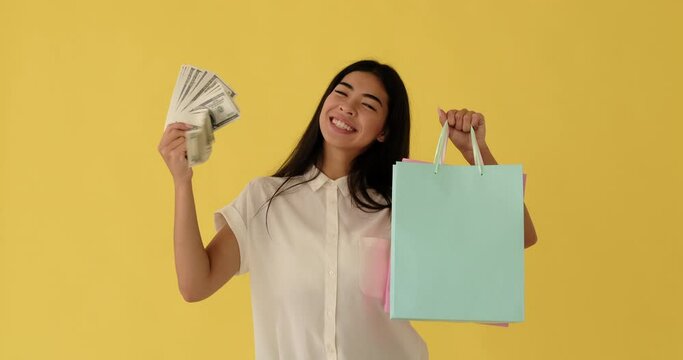 Excited woman holding bundle of dollar banknotes and showing her shopping bags