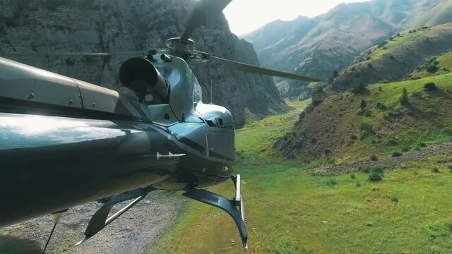 The helicopter flies over a mountain lake and lands on the grass. View from the tail of the helicopter in 4K